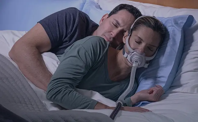 Ett par som sover tätt tillsammans i sängen, kvinnan använder en AirFit F40 PAP-mask.