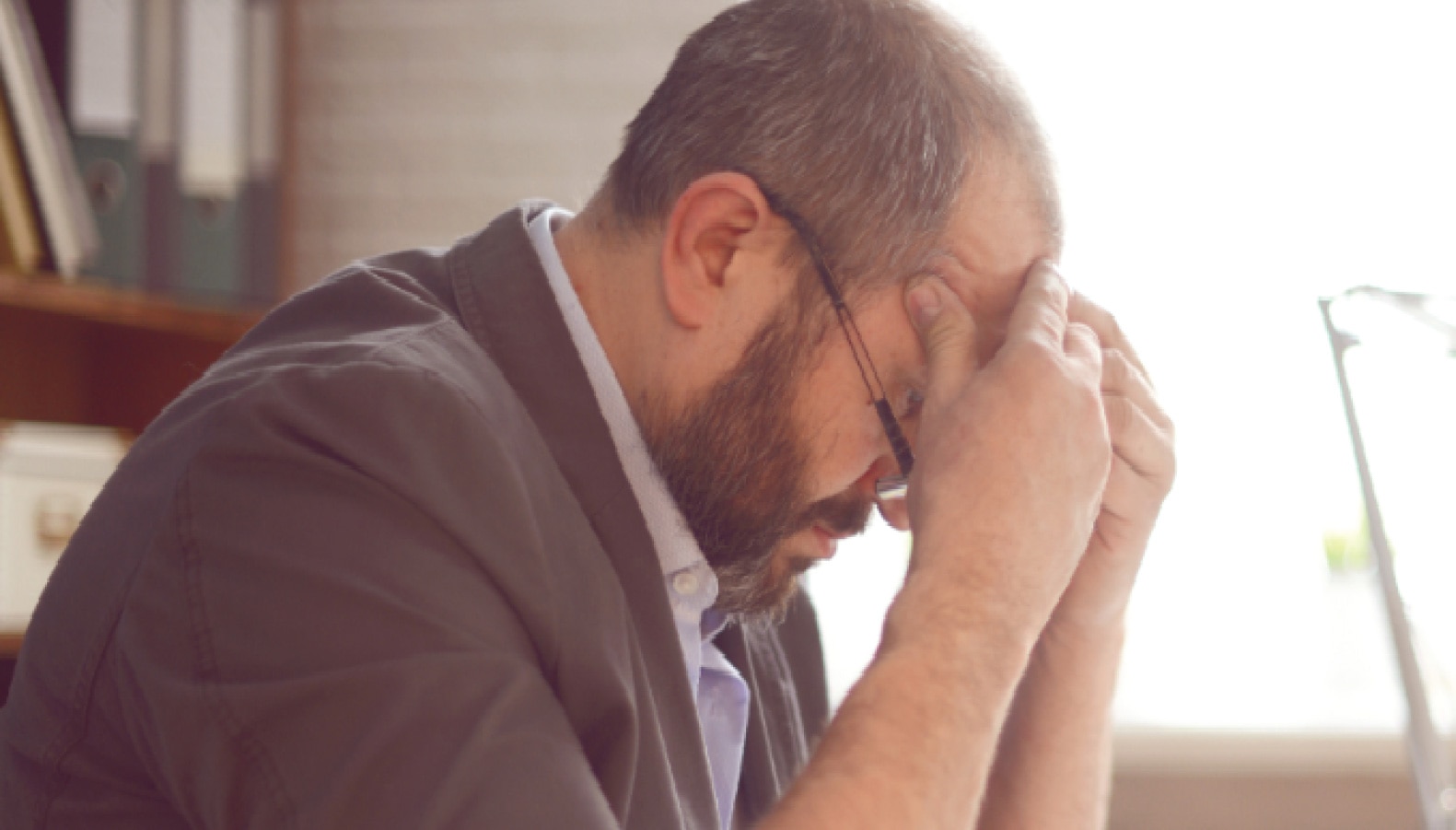 Man med glasögon som lutar över ett bord med ett stressat uttryck